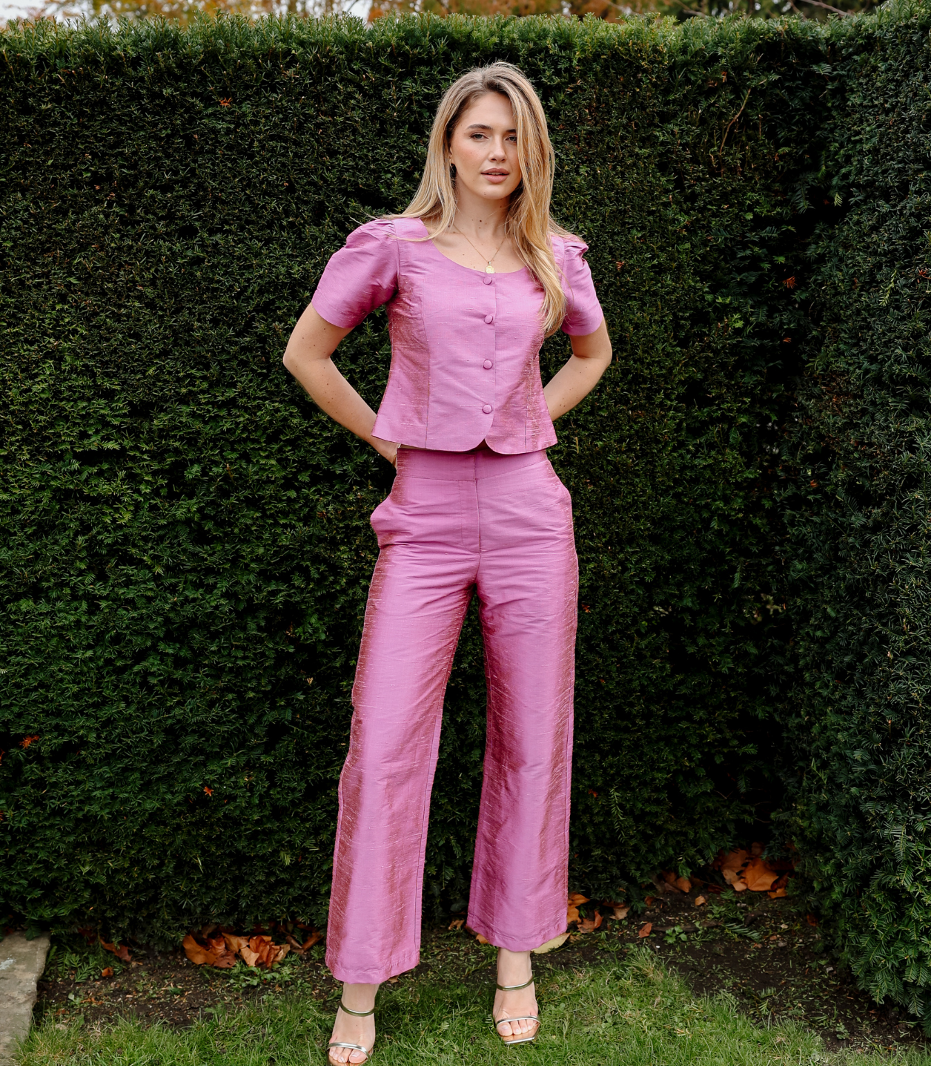 A woman wearing the Jane Top in Lychee, a pink short-sleeve button-down top with a square neckline, paired with matching wide-leg trousers.