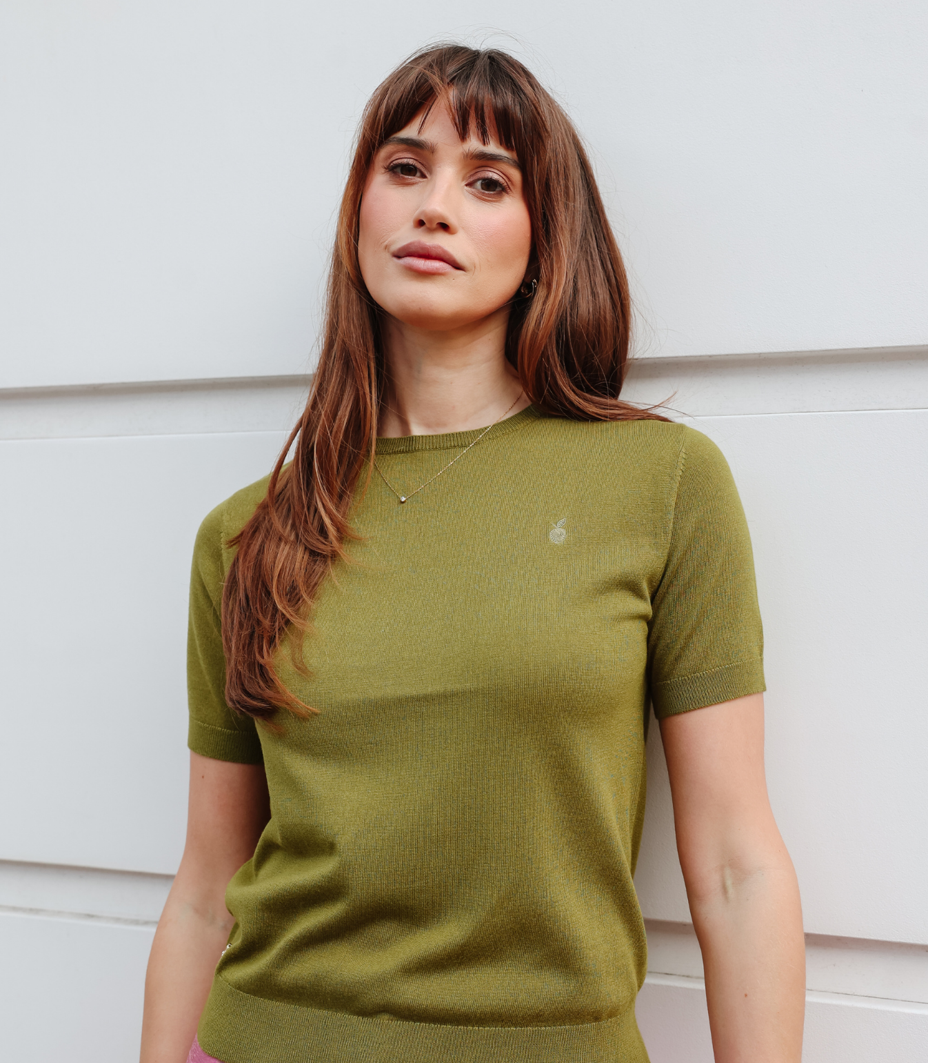 A woman wearing the Kate Knit Top in olive green, a short-sleeve fine knit sweater with a round neckline, paired with pink silk trousers.